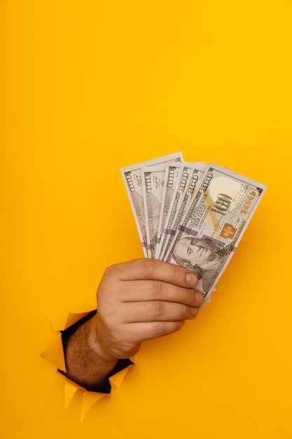 Hand holding money through hole in yellow paper wall Vertical image