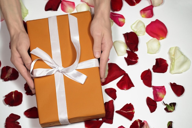 Hand holding orange gift box with rose petals