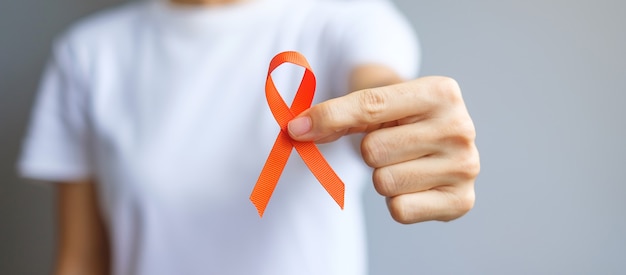 Hand holding Orange Ribbon for Leukemia, Kidney cancer day, world Multiple Sclerosis, CRPS, Self Injury Awareness month. Healthcare and word cancer day concept