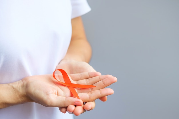 Hand holding Orange Ribbon for Leukemia, Kidney cancer day, world Multiple Sclerosis, CRPS, Self Injury Awareness month. Healthcare and word cancer day concept