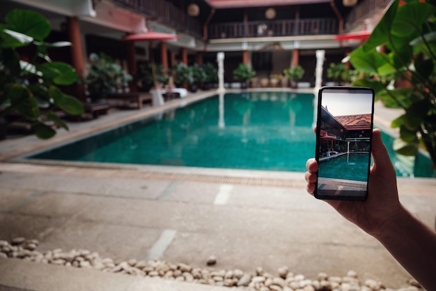 Hand holding phone on background of the pool in hotel