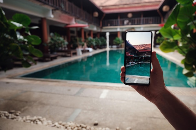 Hand holding phone on background of the pool in hotel