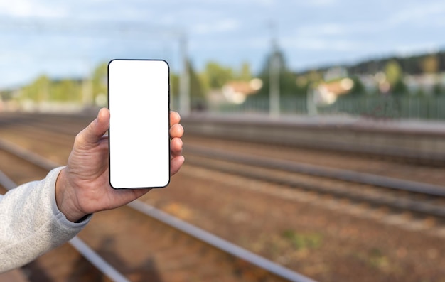 Hand holding phone mockup on railway background with copy space Mobile application with online train timetable Smartphone template with empty display