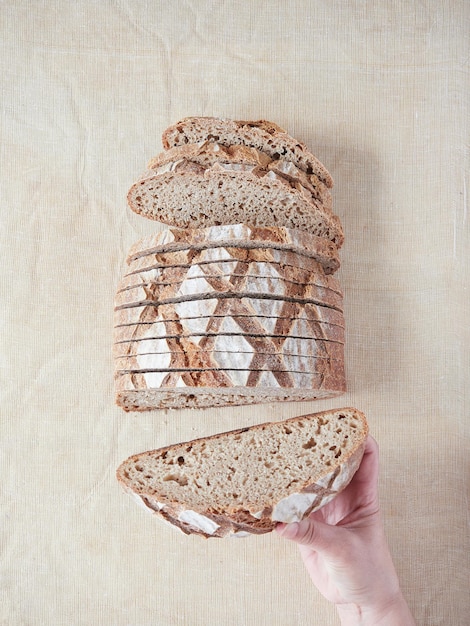 Hand holding a piece of artisan sourdough bread showing the well fermented honeycombed crumb interior Top view on creamcolored linen surface