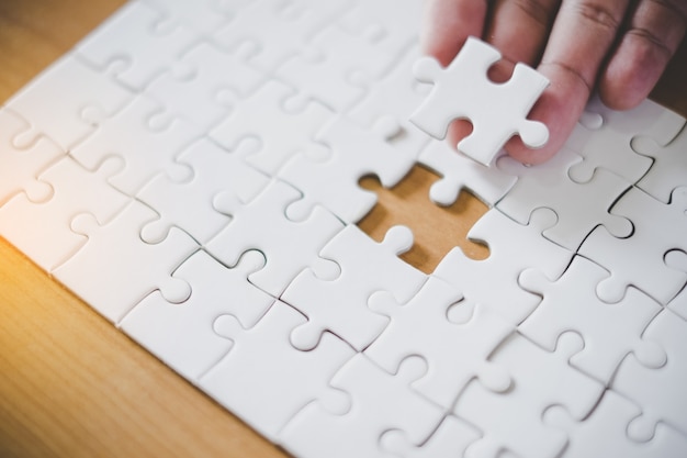 Hand holding piece of blank jigsaw puzzle with paper frame background