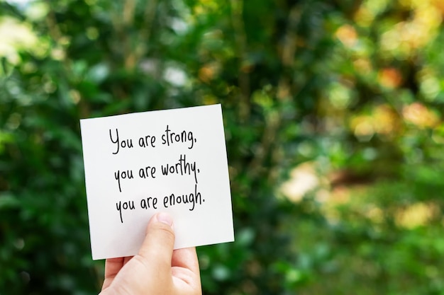 Photo hand holding piece of paper with text you are strong your are worthy you are enough