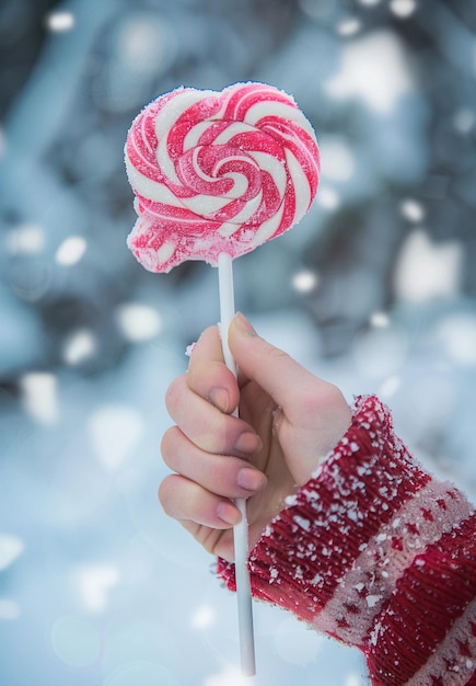 Photo a hand holding a pink lollipop that is in front of a snowy background