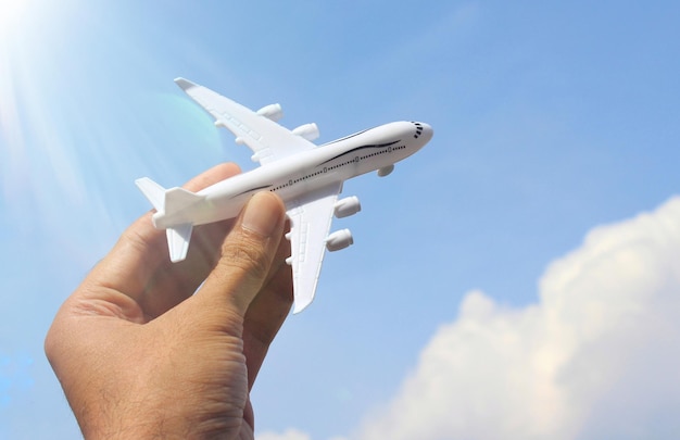 Hand holding plane with background of blue sky and white clouds