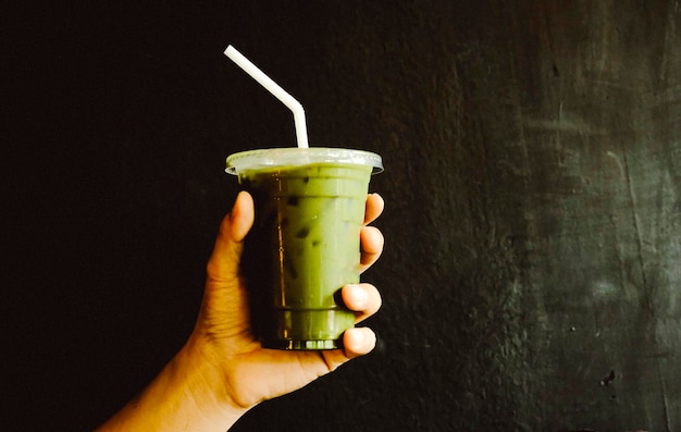 Hand holding a plastic cup of matcha green tea dark background