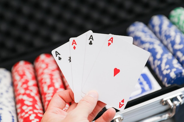 a hand holding a poker chips in front of a rack of playing cards.