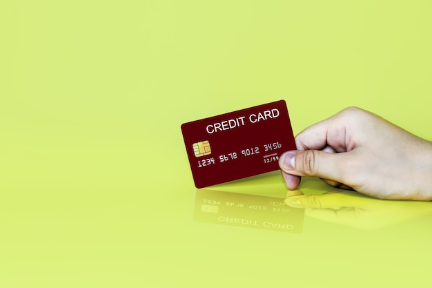 Hand holding a red credit card on a yellow background, credit card can be used to pay for goods or services, credit card concept. Credit card clipping path.