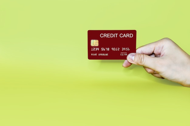 Hand holding a red credit card on a yellow background, credit card can be used to pay for goods or services, credit card concept. Credit card clipping path.