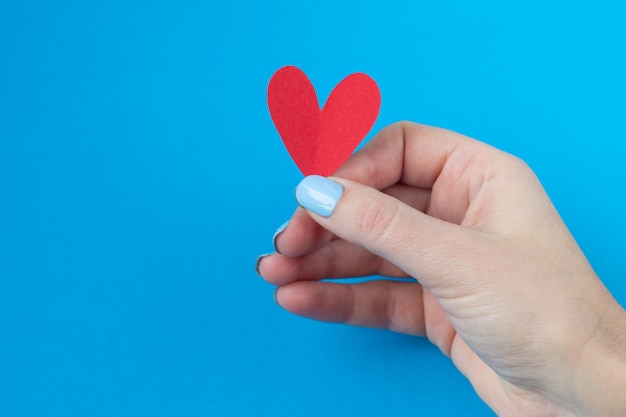 Hand holding a red heart on a blue background. Background for Valentine's day