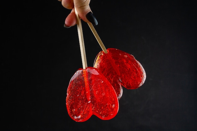 Hand holding red heart candies on black background pair of sweet lollipops