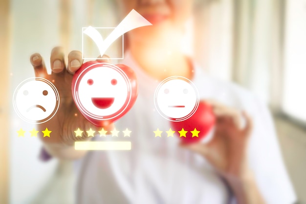 A hand holding red heart for check mark face emoticon smile on dark backgroundCustomer serviceservice mindservice ratingPhoto concept of satisfaction survey and smiling face icons time