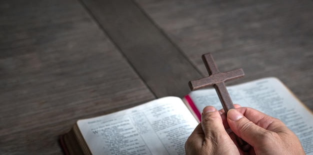 Hand holding religious crucifix cross on top of Holy Bible