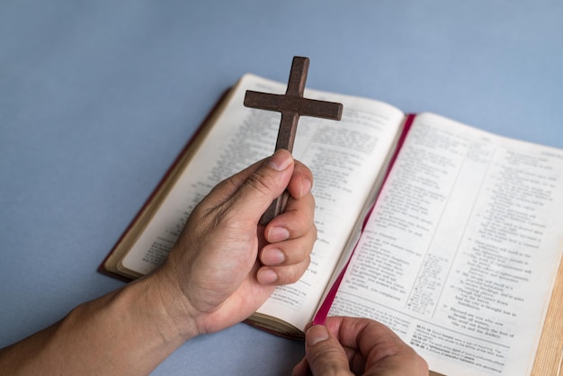 Hand holding religious crucifix cross on top of Holy Bible