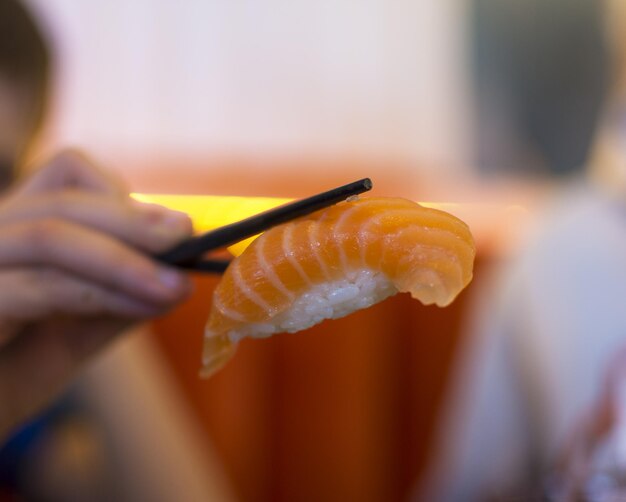 Photo a hand holding salmon nigiri in a sushi restaurant with chopsticks