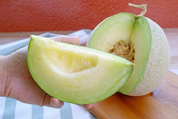 Hand Holding a Slice of Fresh Ripe Juicy Muskmelon Cut from Whole Fruit