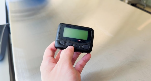 A hand holding a small black device with a green screen.