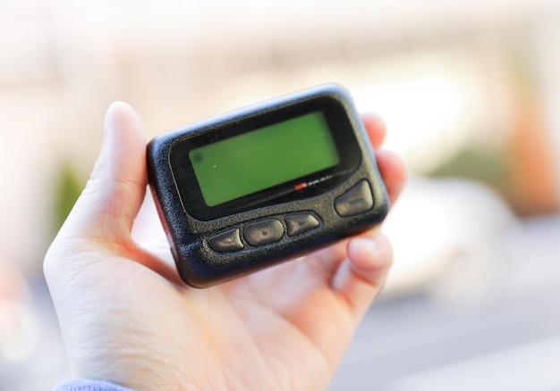 A hand holding a small device with a green screen on it.