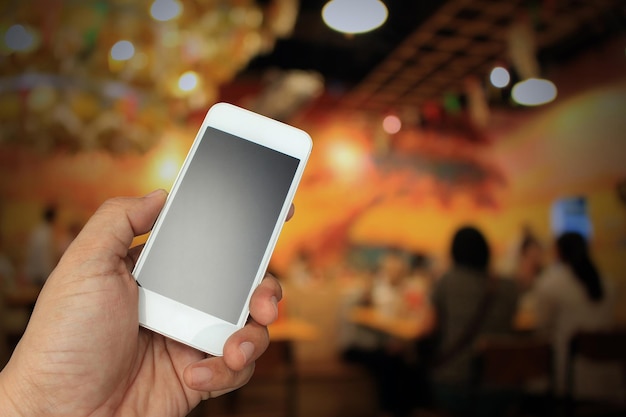 Hand holding the smartphone on blur restaurant background