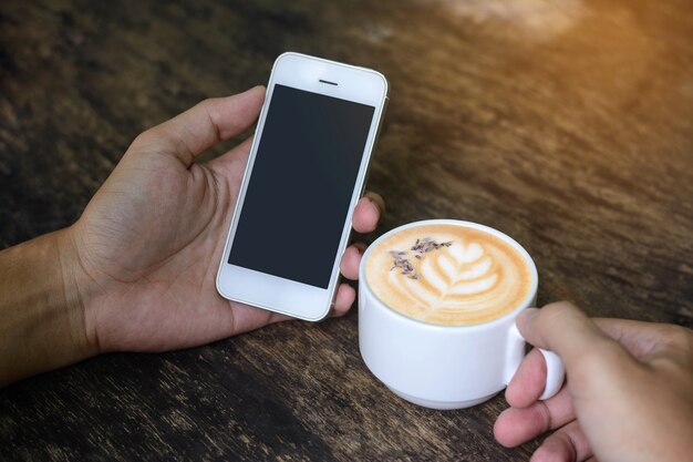 Hand holding smartphone and holding coffee cup on old wooden table