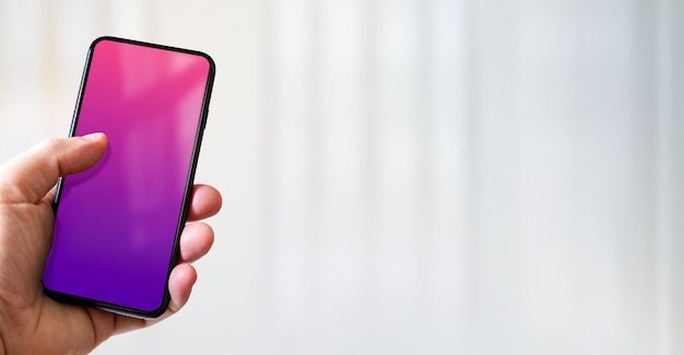 Hand holding a smartphone with blank pink and purple screen Office background Horizontal banner