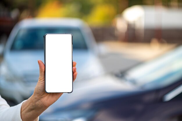 Hand holding smartphone with blank screen defocused cars in background concept of online services