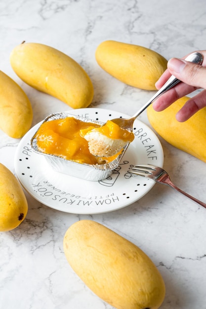 Hand holding a spoon scooped up the mango cheese pie Mango Cheese Pie is packaged in a square aluminum foil in a white plate on a marble table cake in cafe or bakery shop