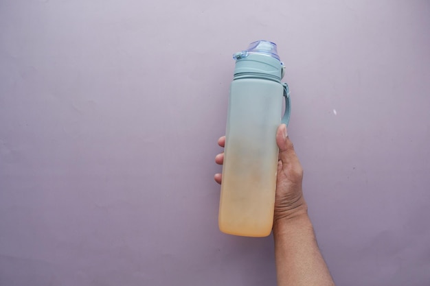 Hand holding sport bottle on purple background