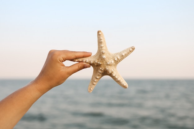 Hand holding starfish with beautiful tropical summer sand beach island, relaxing vacation summer blue sea concept.