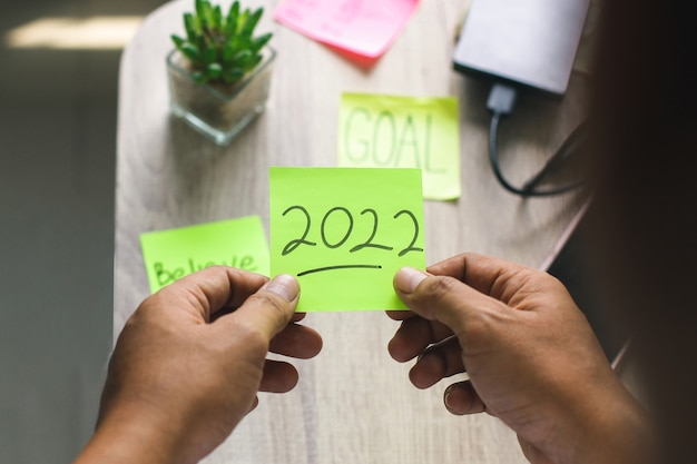 Hand holding sticky notes for welcome new year 2022 with motivational words on the table