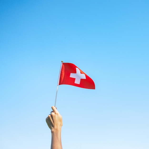 Hand holding Switzerland flag on blue sky background Switzerland National Day and happy celebration concepts