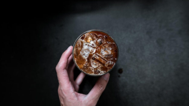 Hand holding a take-out iced coffee on black table