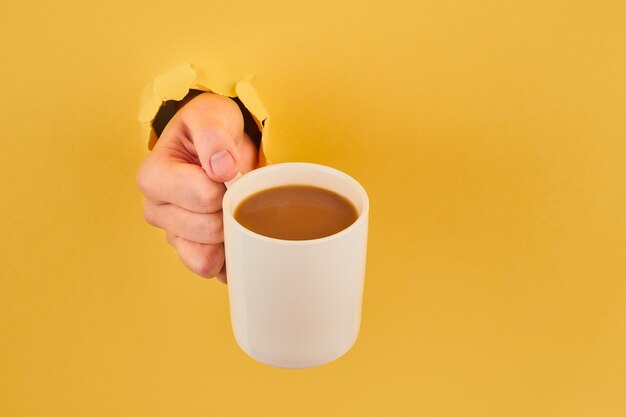 Photo hand holding tea cup against yellow background