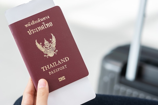 Hand holding Thailand passport and boarding pass ticket with luggage bag.