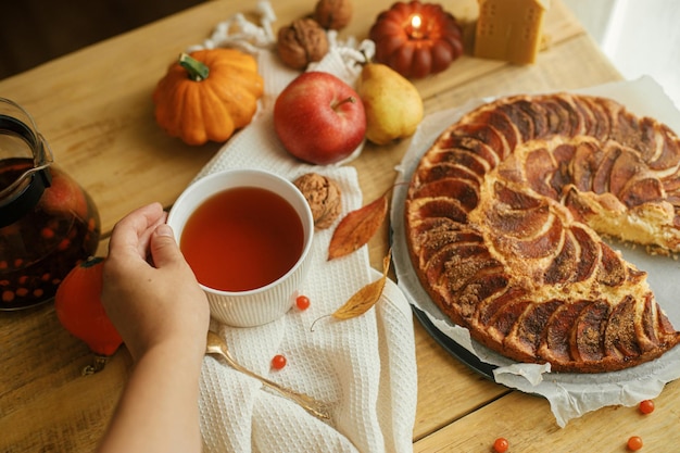 Hand holding warm tea in stylish cup on rustic table with freshly baked apple pie Autumn hygge