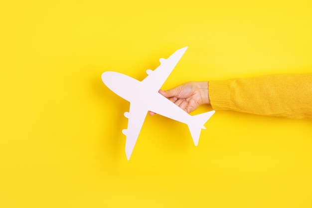 Hand holding white airplane over yellow background