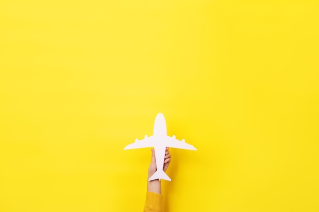 Hand holding white airplane over yellow background