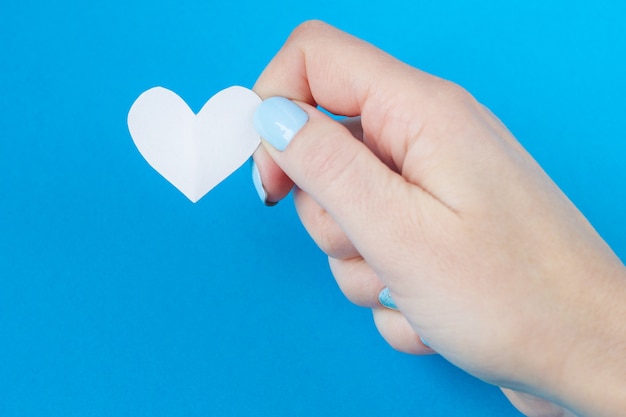 Hand holding a white heart on a blue background