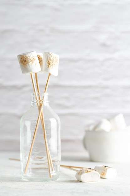 A hand holding a white marshmallow dripping chocolate into a cup on white background.