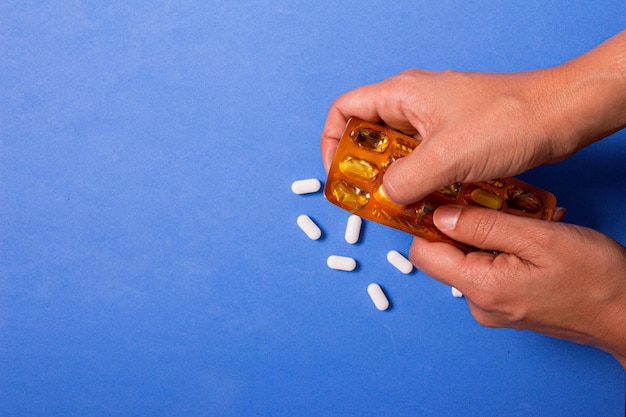 Hand holding white pills on blue background. Copy space.