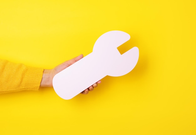 Hand holding white wrench, repair symbol in hand over yellow background