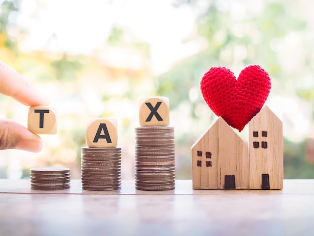 Hand holding wooden block with word TAX on coins. The concept of paying tax for house and property