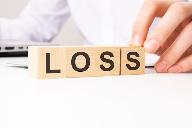 Hand holding wooden cube with LOSS text on table background financial marketing and business concepts