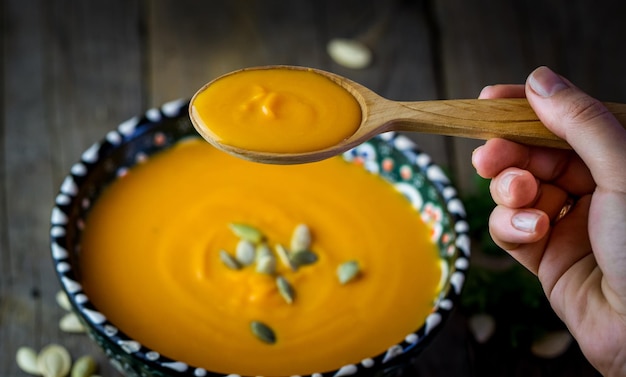 Hand holding wooden spoon with pumpkin soup