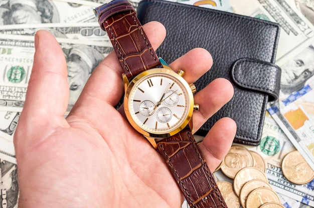 Hand holding wrist watch on background of dollars and wallet