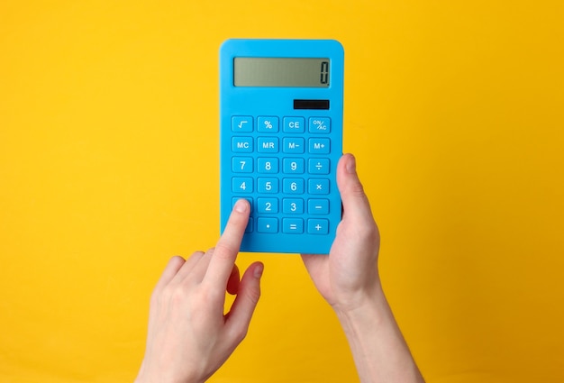 Hand holds blue calculator on yellow.