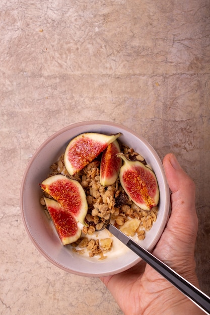 Hand holds a bowl with yogurt, muesli, figs place for text